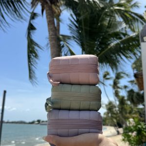 Three allour pouches stacked in a hand on a palm-lined beach