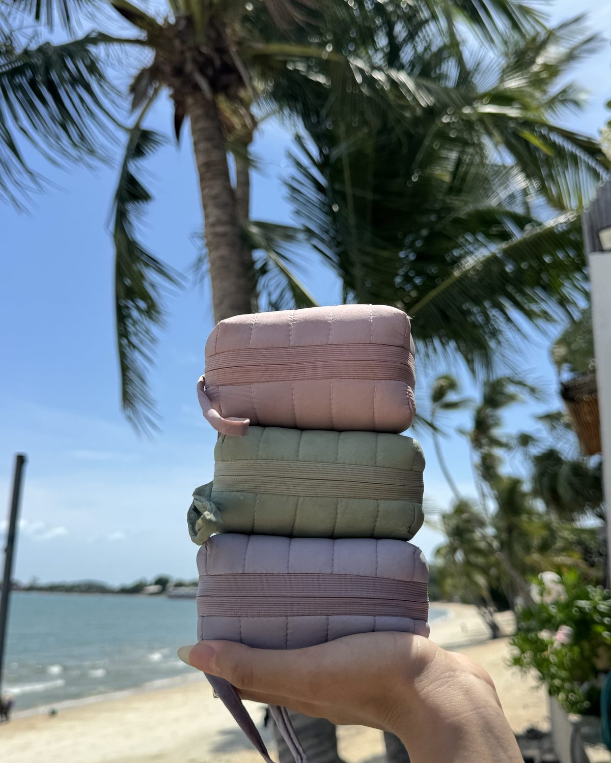 Three allour pouches stacked in a hand on a palm-lined beach